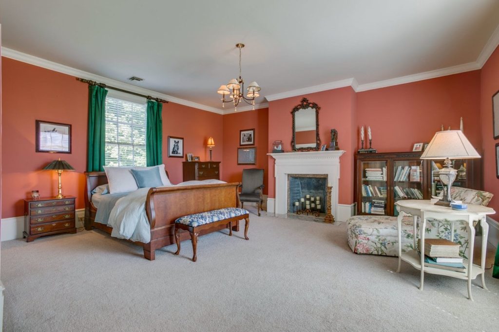 Spacious master bedroom with green curtains, an ornate marble fireplace adorned with mirror, fainting couch, and plush white carpeting.