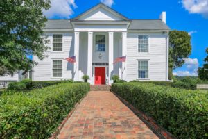 Large two-story Antebellum style home with a red front door, white exterior and columns.