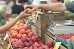 A vendor handing someone an apple at a farmers market