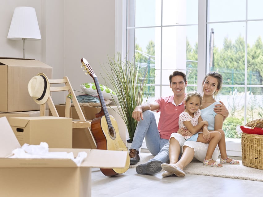 A happy family sitting on the floor of their new living room, surrounded by moving boxes.